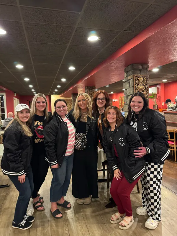 Bestie Squad women in matching smiley bomber jackets together at a restaurant.