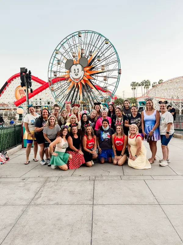 A big group of Bestie Squad women posing together in front of a Ferris wheel at a theme park.