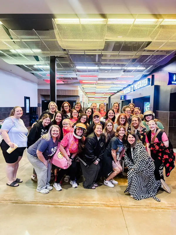 A big group of Bestie Squad women posing together in a movie theater lobby.